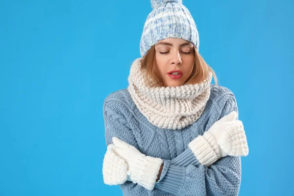 Frozen young woman in winter clothes on blue background