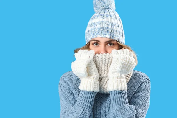 Donmuş genç kadın mavi arka planda kışlık giysiler içinde, yakın plan.