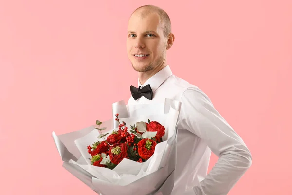 Young man with bouquet of flowers on pink background. Valentine\'s Day celebration