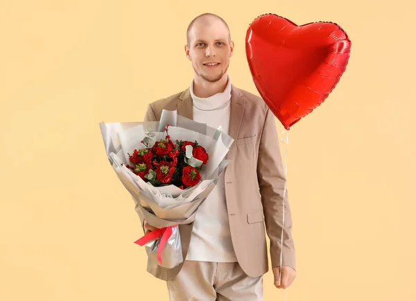 Young man with bouquet of flowers and balloon on beige background. Valentine\'s Day celebration