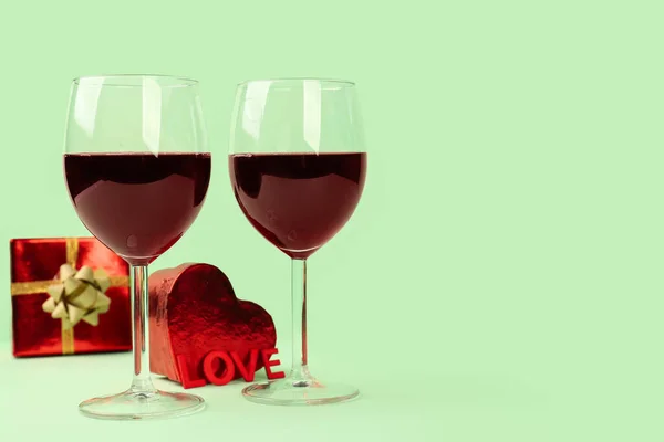 Glasses of wine, word LOVE and gifts on green background. Valentine\'s Day Celebration
