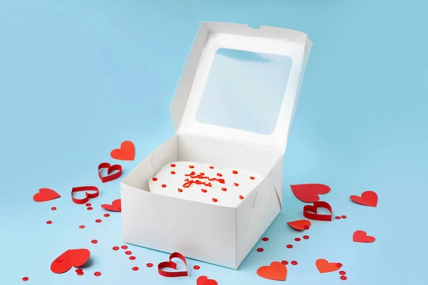 Opened box with tasty bento cake and hearts on blue background. Valentine\'s Day celebration