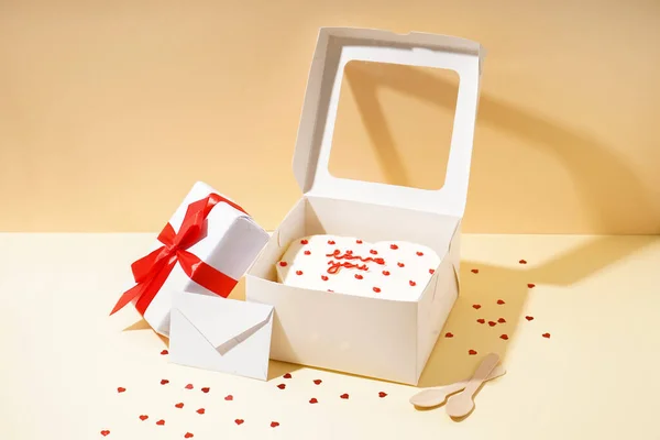 Opened box with tasty bento cake, gift and envelope on beige table. Valentine\'s Day celebration
