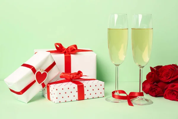 Glasses of champagne, gift boxes and rose flowers on green background. Valentine\'s Day celebration