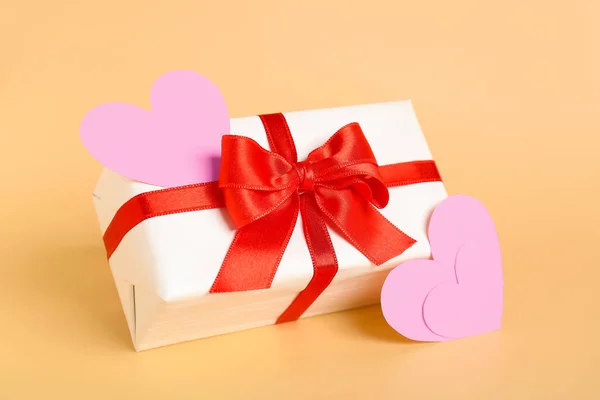 Gift bow with beautiful bow and paper hearts on beige background. Valentine\'s Day celebration
