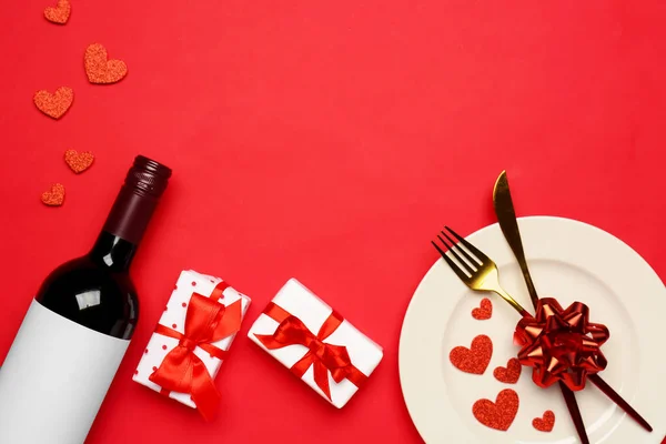 Table setting with gift boxes and bottle of wine on red background. Valentine\'s Day celebration
