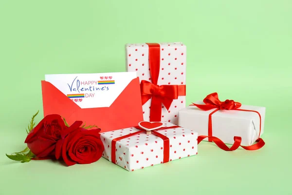 Gift boxes, rose flowers and card with text HAPPY VALENTINE\'S DAY in envelope on green background. LGBT concept