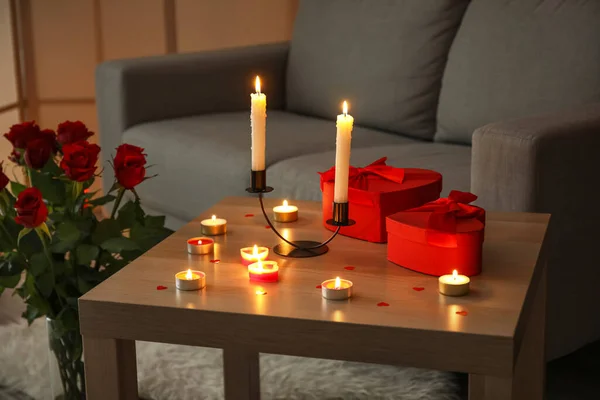 Burning candles and gifts for Valentine\'s Day on table in dark living room