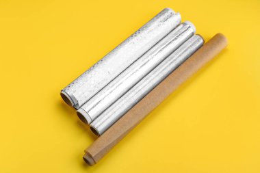 Rolls of aluminium foil, baking paper and food film on yellow background