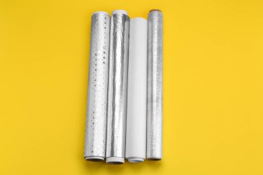 Rolls of aluminium foil, baking paper and food film on yellow background