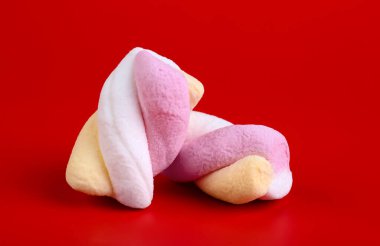 Tasty twisted marshmallows on red background