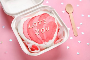Plastic lunch box with heart-shaped bento cake on pink background. Valentine's Day celebration