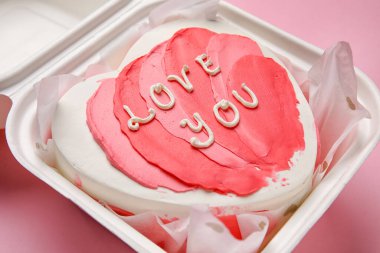 Plastic lunch box with heart-shaped bento cake on pink background, closeup. Valentine's Day celebration