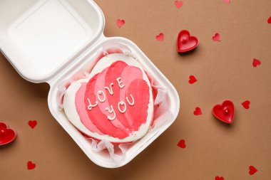 Plastic lunch box with heart-shaped bento cake and candles on brown background. Valentine's Day celebration