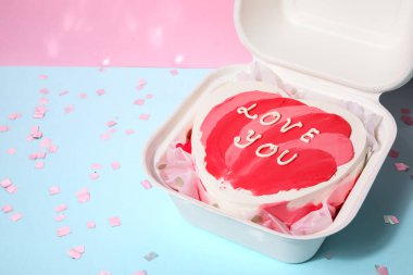 Lunch box with heart-shaped bento cake and confetti for Valentine's Day on table near pink wall