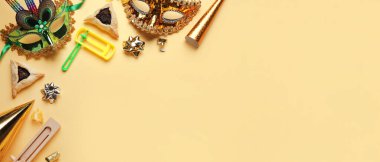 Hamantaschen cookies, carnival masks and rattles for Purim holiday on yellow background with space for text