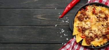 Tasty Mexican dish with nachos on dark wooden background with space for text