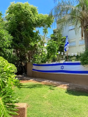 House with fence, flags of Israel and green trees
