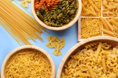 Bowls with different types of raw pasta on light background, closeup