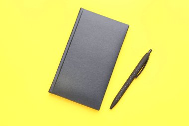Black notebook and pen on yellow background