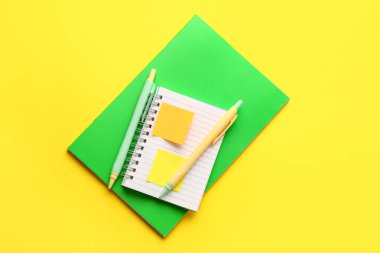Notebooks, pens and sticky notes on yellow background