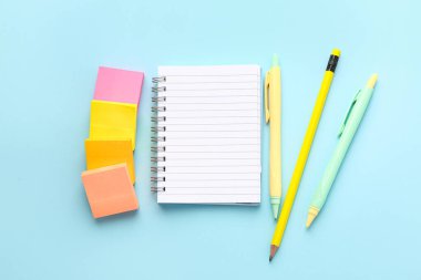 Notebook, sticky notes, pencil and pens on color background
