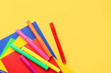 Notebooks and felt-tip pens on yellow background