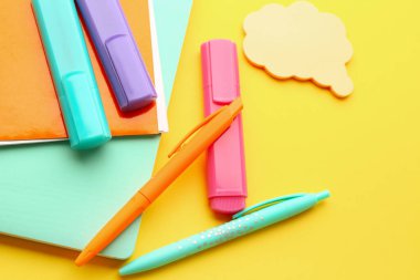 Notebooks, pens, markers and sticky notes on yellow background, closeup
