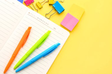 Notebook, pens, sticky notes and paper clips on yellow background, closeup