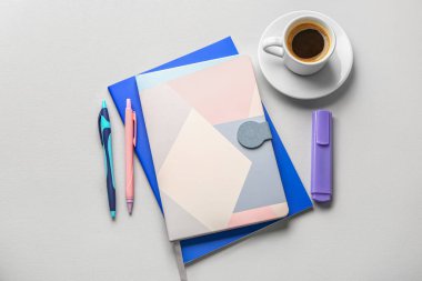 Notebooks, pens, marker and cup of coffee on light background