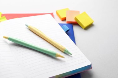Notebooks, pens and sticky notes on light background, closeup