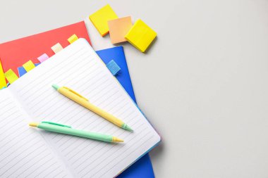 Notebooks, pens and sticky notes on light background, closeup