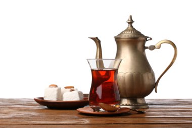 Cup of Turkish tea, teapot and sweets on wooden table against white background