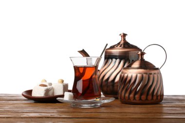Cup of Turkish tea, teapot, sugar bowl and sweets on wooden table against white background