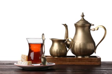 Cup of Turkish tea with sweets, teapot and milk jug on wooden table against white background
