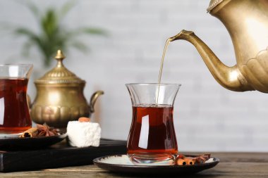 Pouring of hot Turkish tea from teapot into glass on wooden table