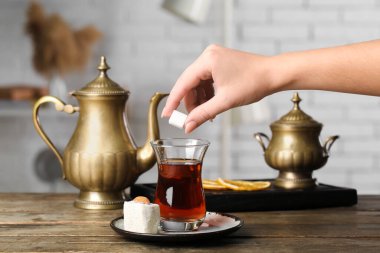 Woman putting sugar into cup of Turkish tea on wooden table