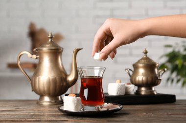 Woman putting sugar into cup of Turkish tea on wooden table