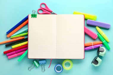 Composition with blank open notebook and different stationery on color background