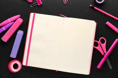 Composition with blank open notebook and colorful stationery on dark background
