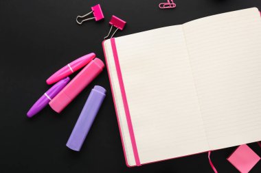 Blank open notebook, markers and binder clips on dark background