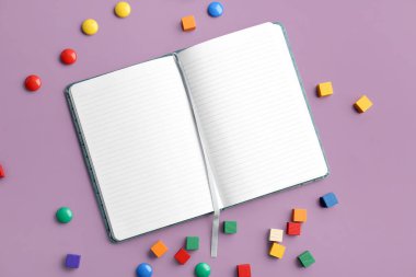 Blank open notebook, colorful magnets and cubes on color background
