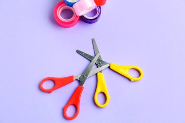Scissors and adhesive tape rolls on lilac background