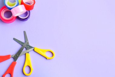 Scissors and adhesive tape rolls on lilac background