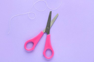 Scissors and thread on lilac background