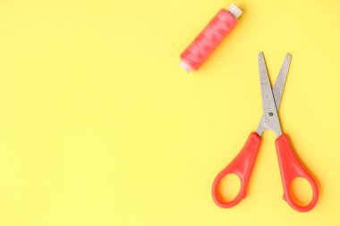 Scissors and thread spool on color background