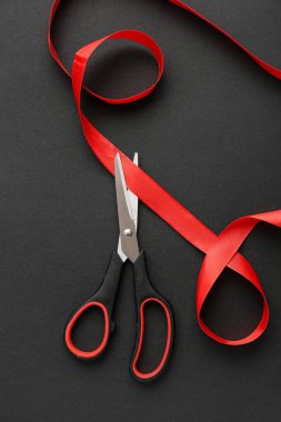 Scissors and red ribbon on dark background