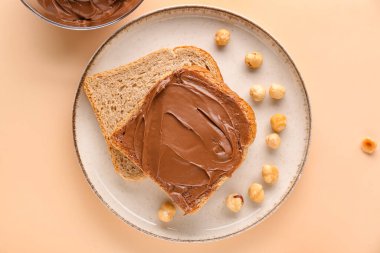 Plate of tasty toasts with hazelnut butter and nuts on color background