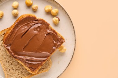 Plate of tasty toasts with hazelnut butter and nuts on color background, closeup