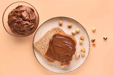 Plate of tasty toasts with hazelnut butter and nuts on color background